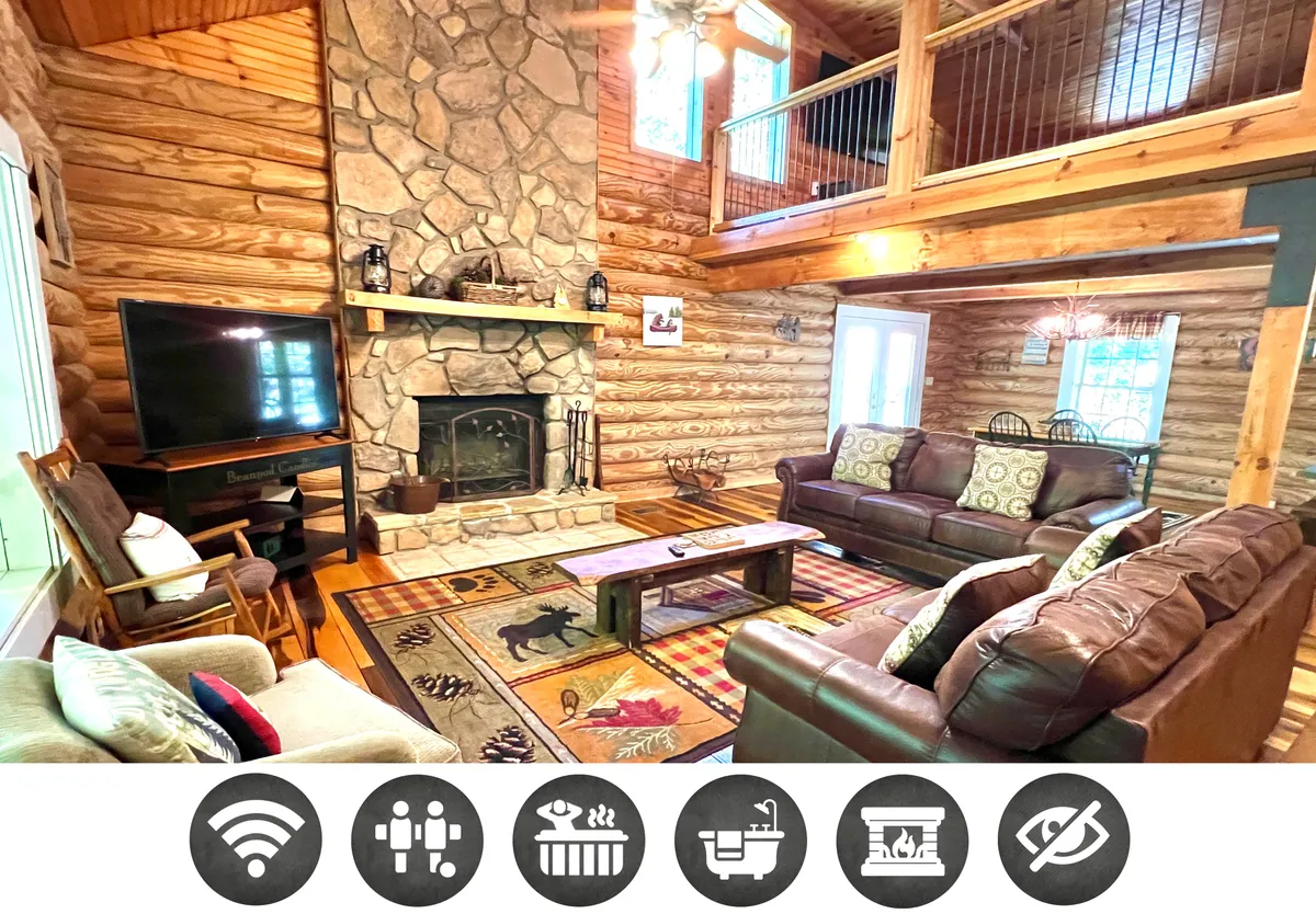 The hero image features a warm, inviting living room with a majestic stone fireplace as the focal point. Rustic wooden beams line the ceiling, complementing the log cabin aesthetic. Plush sofas are arranged for cozy gatherings, and a rug adorned with animal motifs adds a touch of playful mountain charm. Sunlight streams through large windows, bathing the space in a golden glow and offering glimpses of tranquil nature outside.