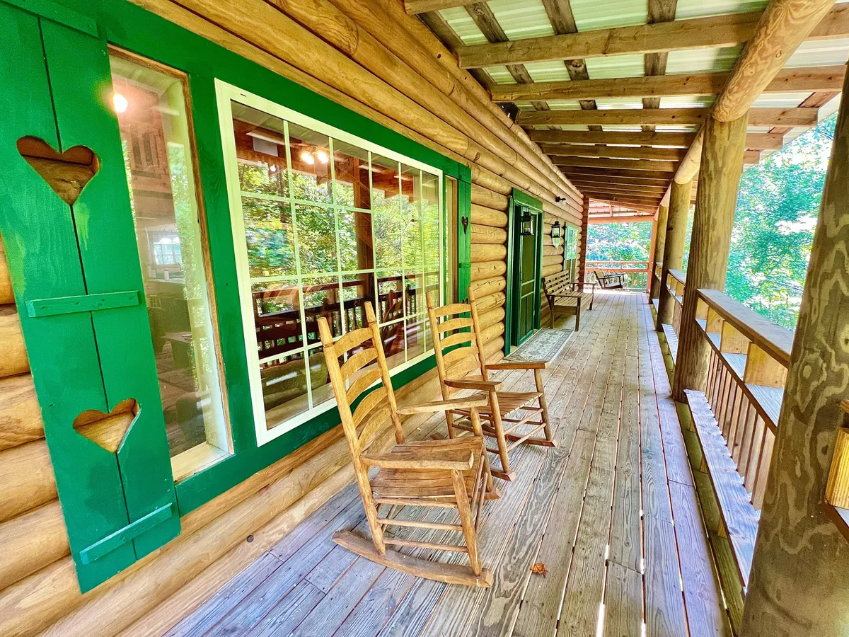 Classic rocking chairs line a shaded porch, with green window shutters and sturdy wooden beams. The scene is tranquil and welcoming, inviting guests to relax, stargaze, or share stories after a day exploring local attractions.