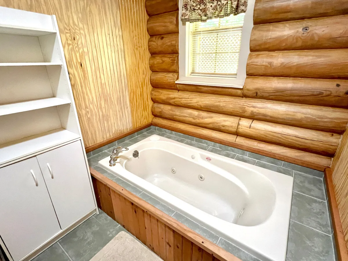 A serene bathroom with a whirlpool jacuzzi tub set against wooden log walls, complemented by a white shelving unit for towels and amenities. The mood is tranquil and spa-like, ideal for relaxation and rejuvenation.
