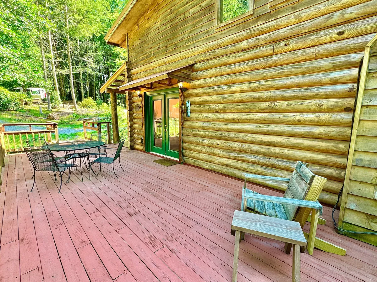 A spacious wooden deck with outdoor seating invites guests to dine al fresco or unwind surrounded by trees. The log cabin's rustic façade and green doors blend seamlessly into the natural setting, offering a tranquil spot to enjoy the mountain air after lively adventures.