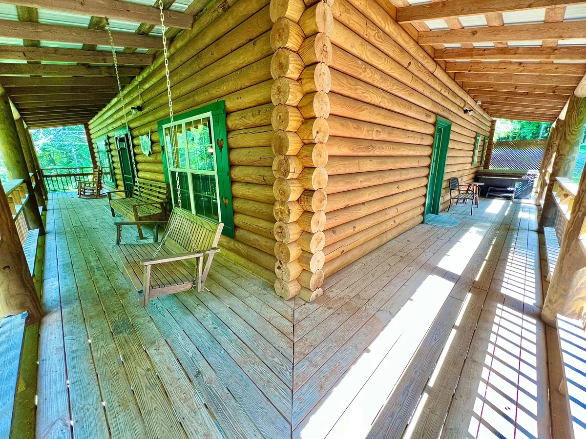 A welcoming porch scene with rocking chairs and wooden log walls, set against green-trimmed windows. The space exudes a cozy, peaceful mood, perfect for enjoying sunsets or stargazing in any season.