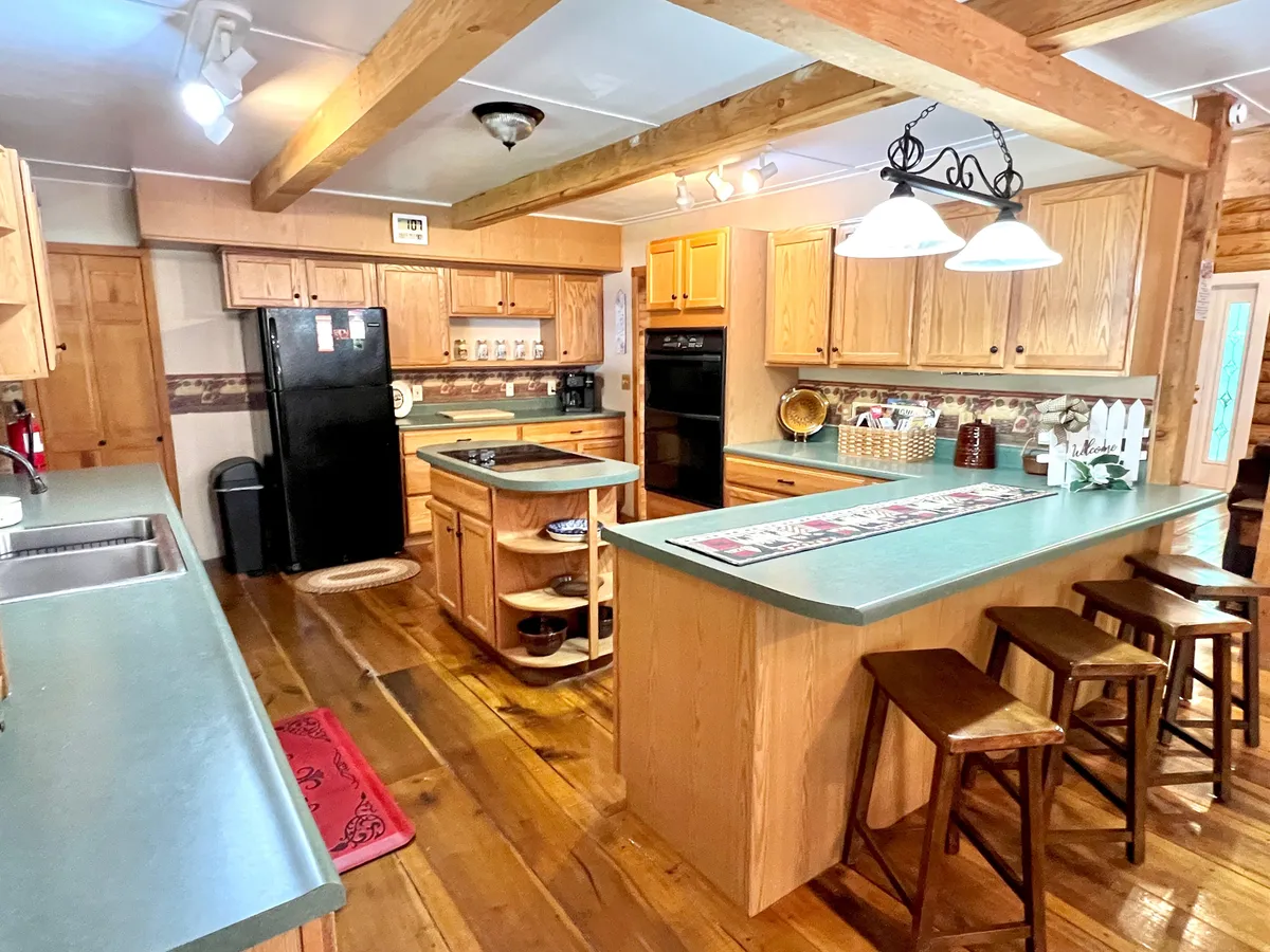 A warm, inviting kitchen featuring a central island with wooden cabinets, modern appliances, and stools at the bar. The space exudes a cozy ambiance, perfect for cooking and casual gatherings, with ample room for meal prep and interaction.