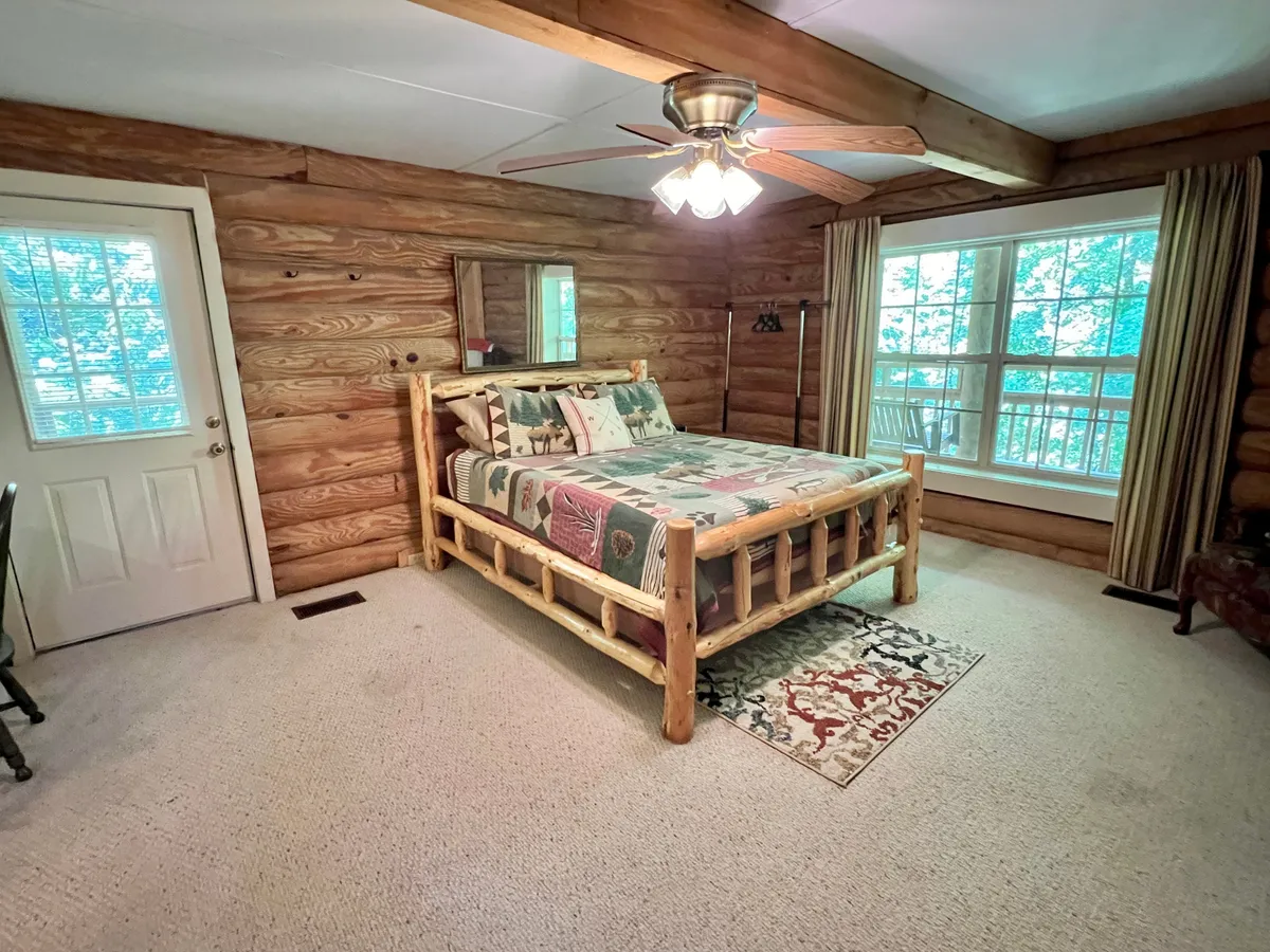 A charming upstairs bedroom featuring a log bed, large window with nature views, a decorative rug, and a mirror. The space feels bright and cozy, perfect for unwinding after a day of adventure.