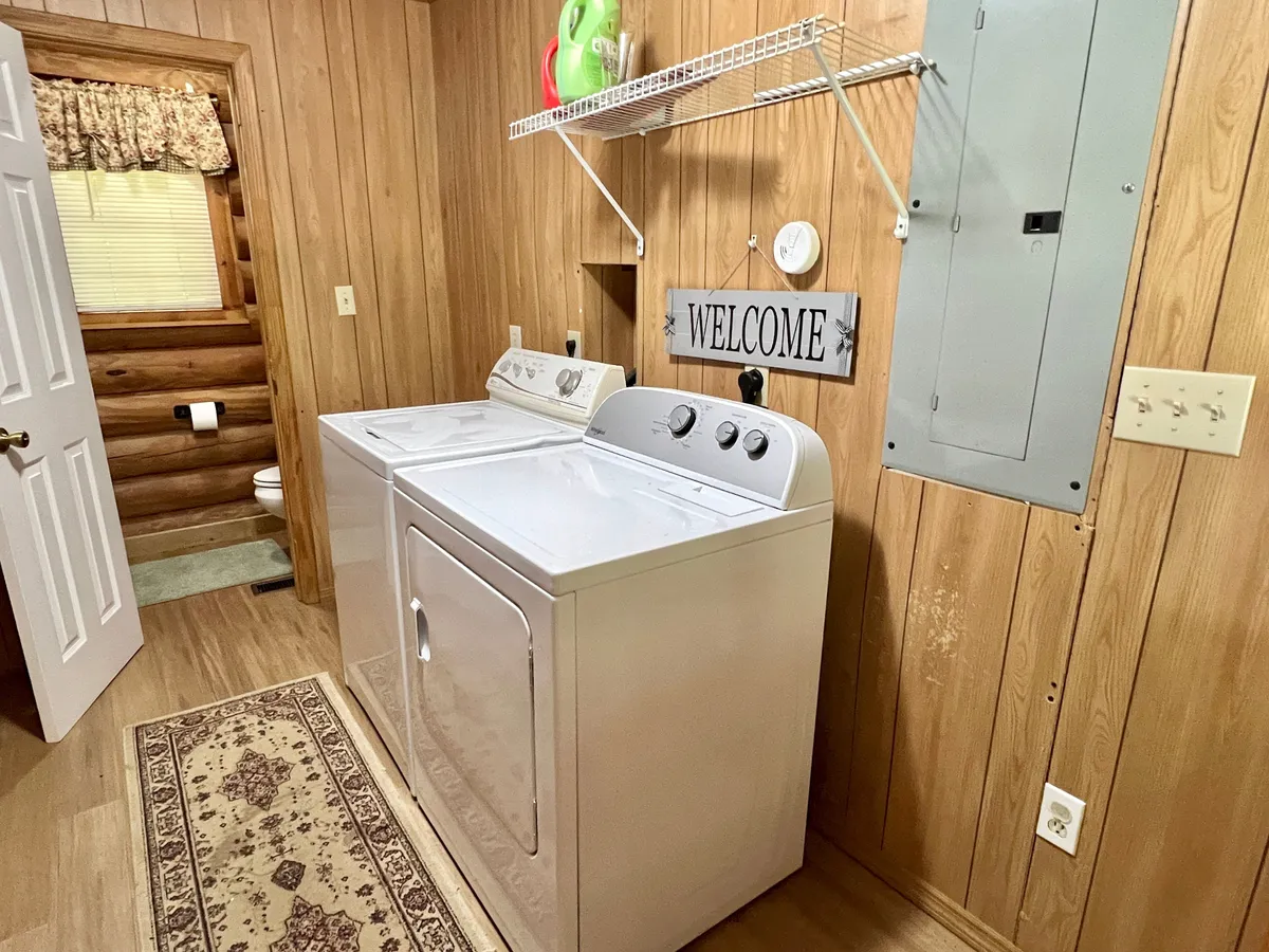 A homey laundry area with a washing machine, dryer, welcome sign, and rustic wood paneling. The space feels practical yet warm, supporting convenient amenities for longer stays.